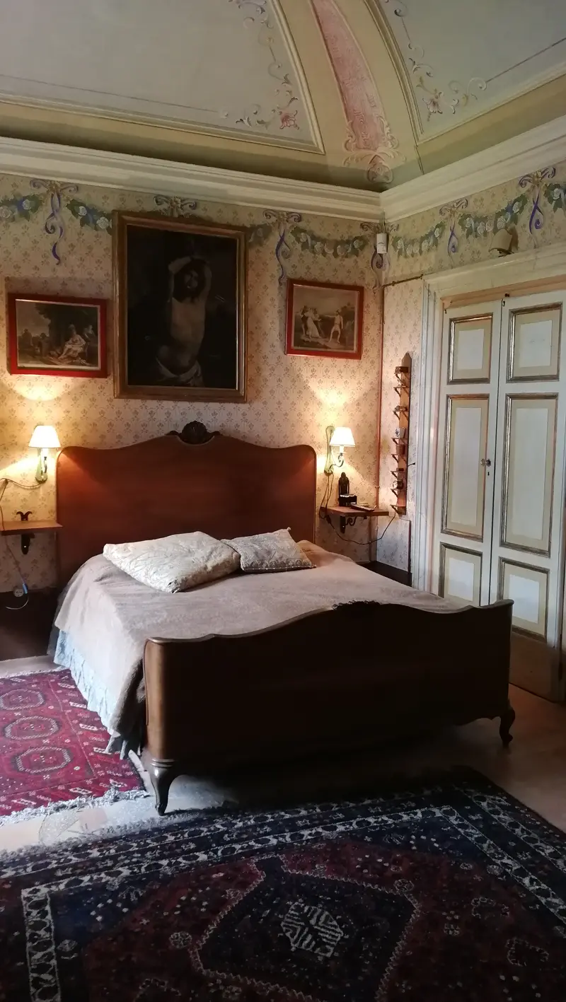 La Camera Marisa: letto in legno sotto la volta affrescata, con fregi floreali dipinti alle pareti e applique accese