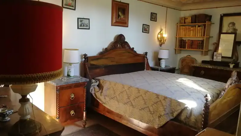 La Camera delle Rose: letto con testiera in legno intagliato e coperta chiara, quadri alle pareti