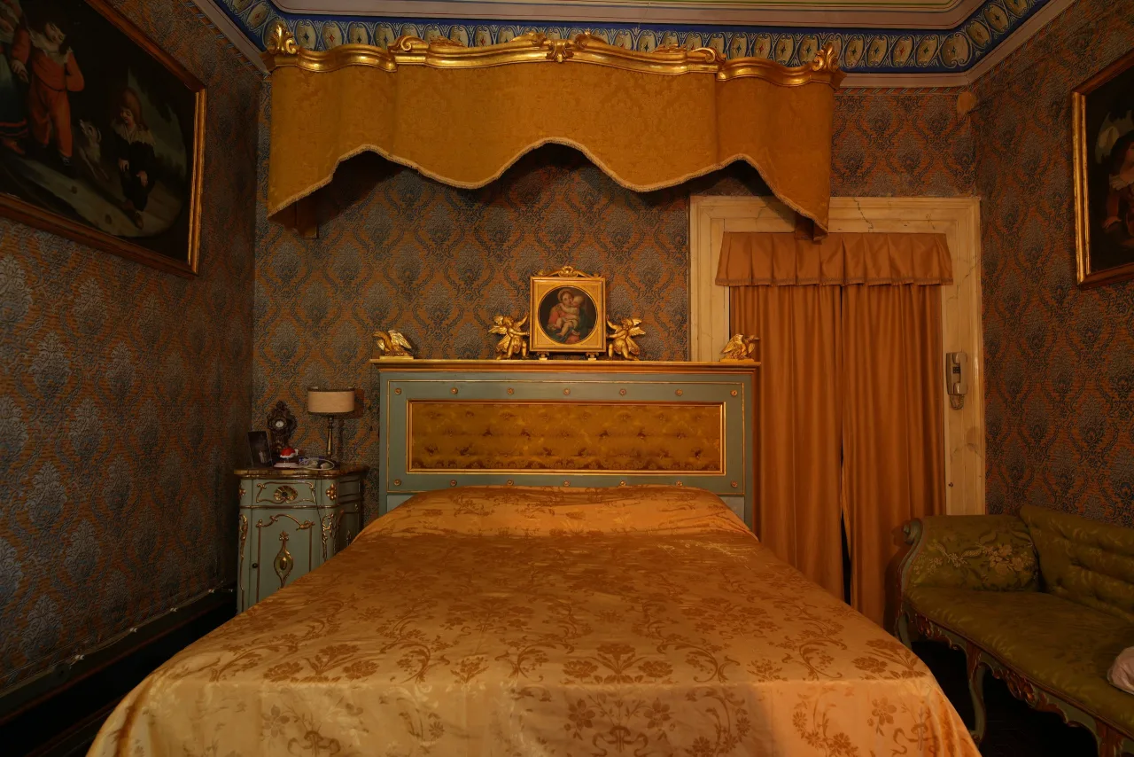 Camera intima con letto a baldacchino dorato, copriletto in damasco oro, parati blu damascati e tendaggi color ambra