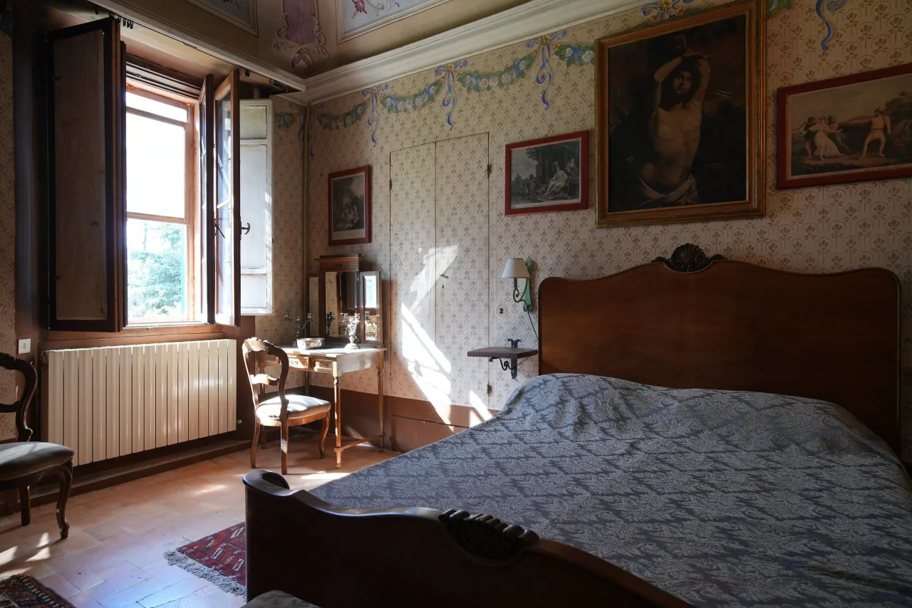 Camera doppia classica con letto in noce, copriletto chiaro, comò con specchiera e ritratto ovale dorato alla parete