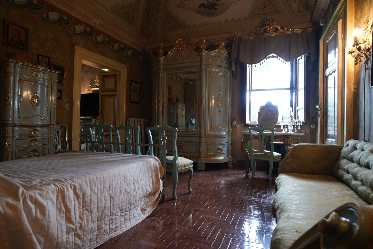 Ampia suite con mobili veneziani laccati verde acqua e dorature, letto, divano e toeletta presso la finestra