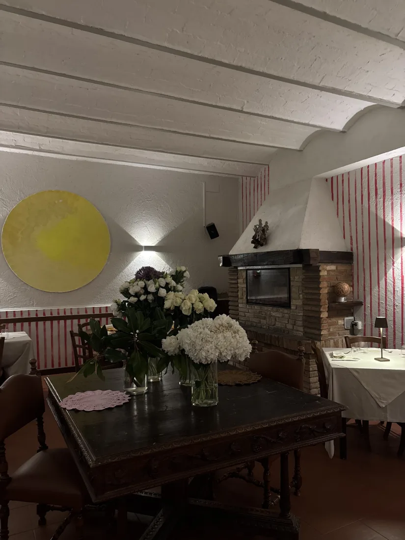 Angolo della sala di Villa Luzi con camino in mattoni, antico tavolo intagliato e composizioni di rose e ortensie bianche