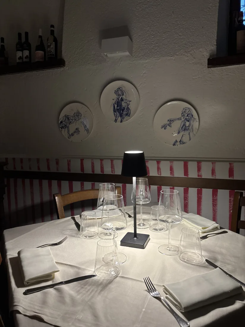 Tavolo apparecchiato con lume e calici sotto tre piatti d'autore dipinti in blu appesi alla parete